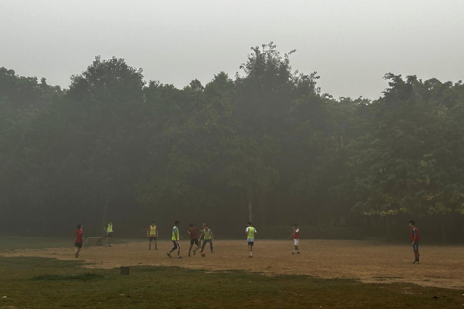 Children playing football early in the morning in a Delhi park covered in smog and fog