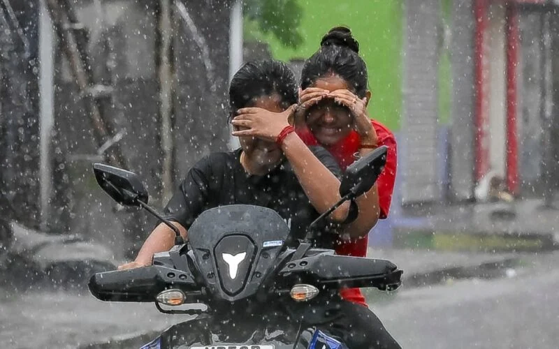 Riders cover their faces while moving on a two-wheeler in the rain